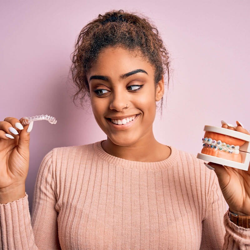 Smiling Young Adult holding clear aligners and teeth diagram with braces