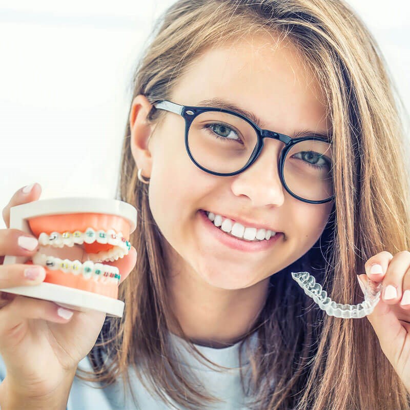 Teenage girl hold clear aligners and teeth with braces